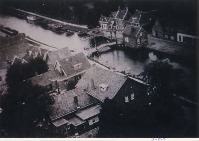 De-brug-over-de-Reevaart
Gezicht op de Voorstraat met de brug over de Reevaart. 
De foto moet genomen zijn voor 1952.
Gebouwen op de voorgrond zijn gesitueerd aan de Dammerweg.
De woning aan de Reevaart naast de brug is de brugwachterswoning. 
De woningen over de Reevaart zijn van links naar rechts
(in 2008) Dhr. O. Haan, A. van Schaik, J. v.d Linden, fietsenwinkel Kroon, Slagerij Vernooij,
bloemenzaak Lidyen daarnaast een kledingzaak.

