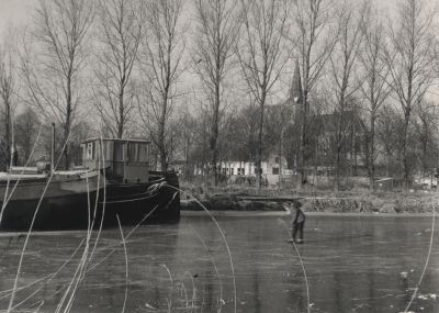 IJs-in-de-Reevaart
Winters dorpsgezicht met op de achtergrond de N H Kerk op de heuvel en er voor de diakonie huizen -  Op de voorgrond een schip en een onbekend schaatsend meisje
Trefwoorden: Dorpszicht